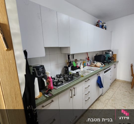 מטבח עם ארונות לבנים ומשטח עבודה ירוק
